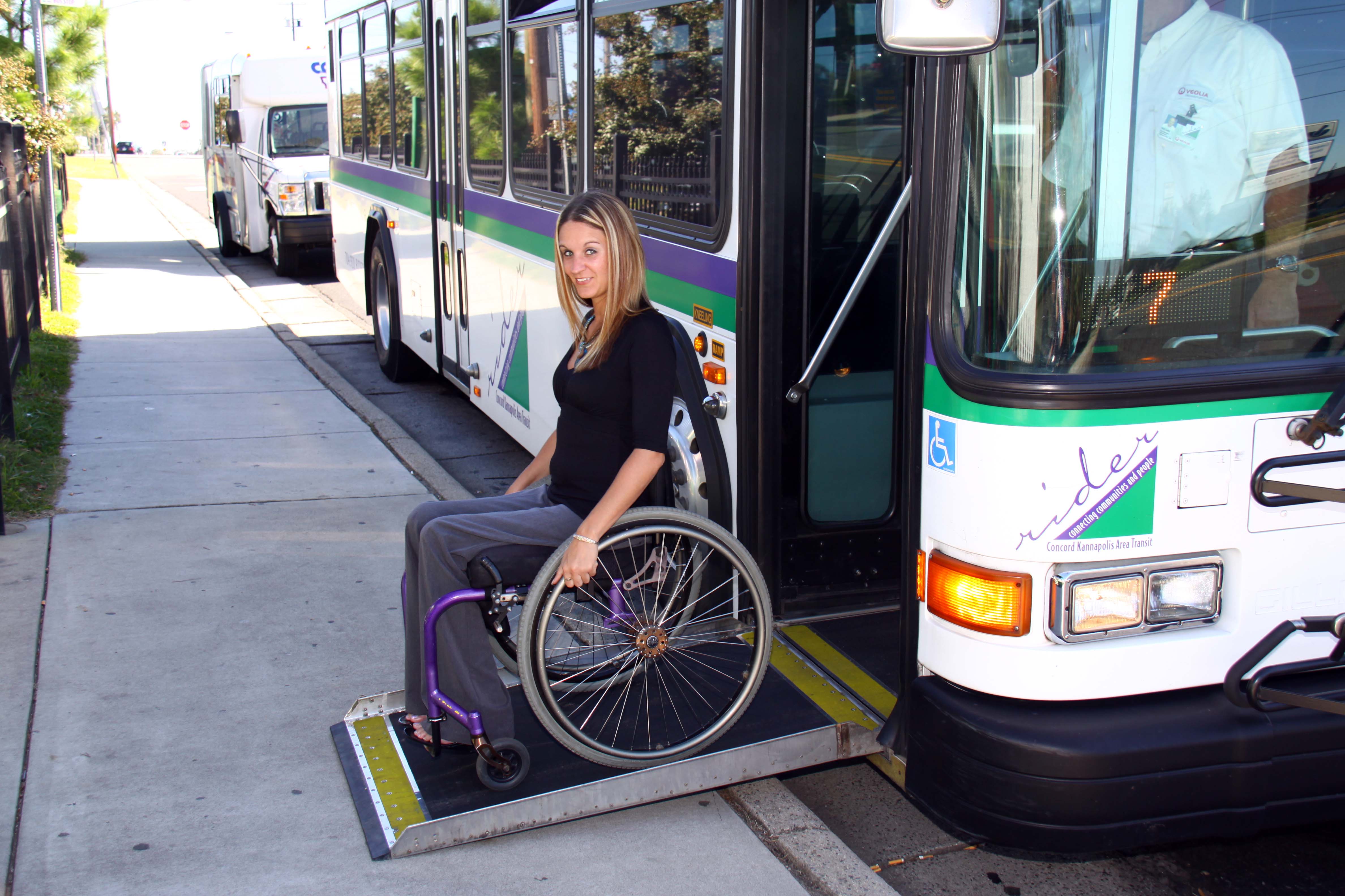 Woman in Manual Wheelchair exiting bus with ramp onto sidewalk.